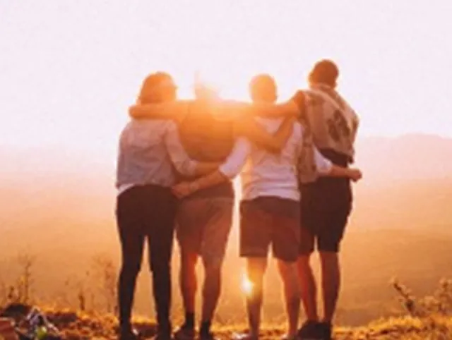 Gruppe Freunde umarmt bei Sonnenuntergang.