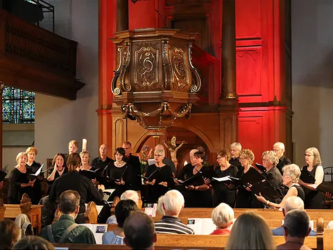 Chor singt in Kirche, Kanzel im Hintergrund.