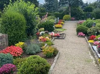 Kiesweg auf einem gepflegten kirchlichen Friedhof mit verschiedenen Pflanzen.
