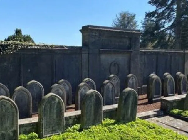 Historische Grabsteine auf einem Friedhof vor Steinmauer.